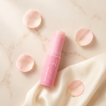 danchel glow balm stick flat-lay on marble with petals